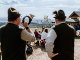 Zwei Jaghornbläser stehen zum Kuhball in Schierke auf einer Wiese und spielen auf ihren Jagdhörnern ein Ständchen.